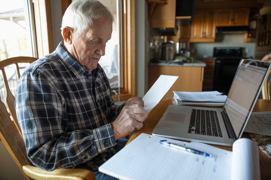 Senior man paying bills at laptop in kitchen