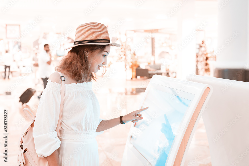 Wall mural happy asian girl using an interactive info touchscreen assistant in the shopping mall.