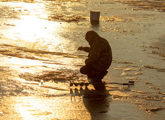 A fisherman catches fish on ice at dawn