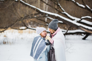 Mother and daughter are walking in the winter forest, wrapped in a blanket, tea or a drink from a thermos