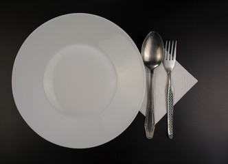 White plate and iron cultery lie on a black table 