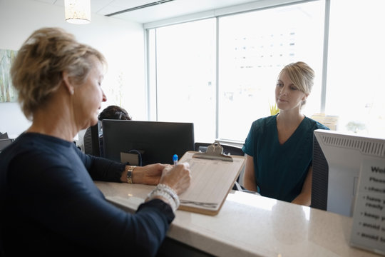 Female Patient Checking In, Filling Out Paperwork At Clinic