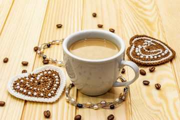 Valentine's Day concept. Cup of coffee, knitted heart, string of pearl beads. Romantic breakfast and gift on wooden boards background