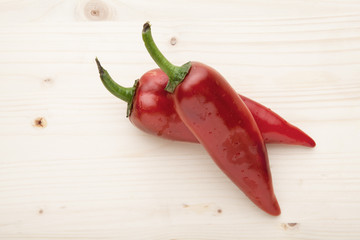 Two red peppers on a wooden background.