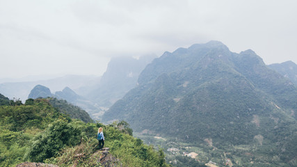 Fototapeta na wymiar Young Caucasian woman standing on the top of the mountain overlooking river valley in Nong Khiaw village, Laos. Solo traveller with backpack