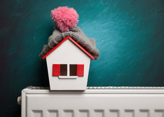 house in winter - heating system concept and cold snowy weather with model of a house wearing a...