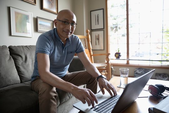 Portrait confident Latinx man using laptop in living room