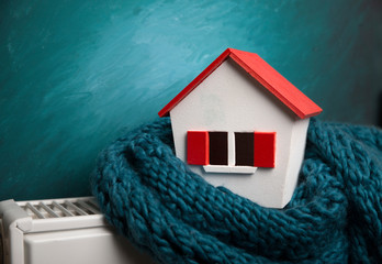 house in winter - heating system concept and cold snowy weather with model of a house wearing a...