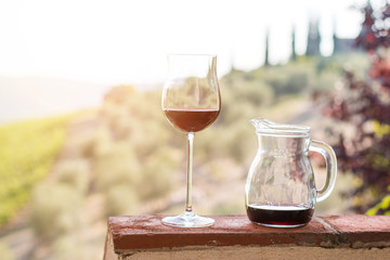 Glass of red wine at Tuscany. Wine yards in the background. Sunshine.