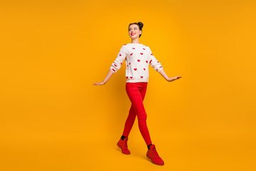 Fototapeta na wymiar Full body profile photo of pretty funny lady walk street cheerful good mood traveler abroad wear hearts pattern sweater red pants shoes isolated yellow color background