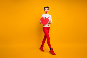 Fototapeta na wymiar Full body photo of pretty funny lady hold paper heart walk street creative idea date invitation boyfriend wear hearts pattern sweater red pants shoes isolated yellow color background