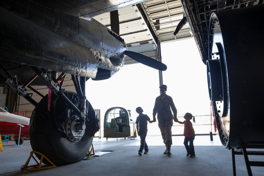 Female army engineer mother walking with children in military airplane hangar