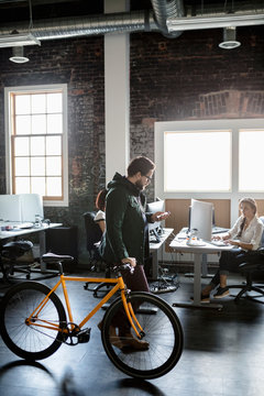 Creative businessman walking bicycle in loft office