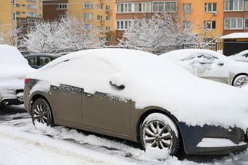 a car covered in snow is parked on a city street among residential buildings during the snowy winter season