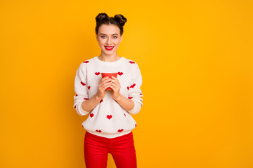 Fototapeta na wymiar Photo of beautiful lady holding hot coffee beverage cup toothy smiling enjoy free time relaxation wear hearts pattern white sweater red pants isolated yellow color background