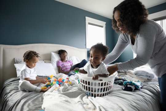 Playful mother placing baby son in laundry basket on bed
