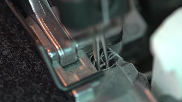Overlock Sewing Machine. Close up stitches in slow motion. Machine serging the edges of fabric. Presser feet