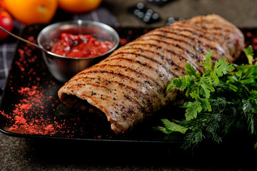 Top view delicious steak. Cooked Pork Loin Roast, red bbq sauce, greens with vegetables and spices on black stone background. Grilled meat, tasty barbecue ketchup, rustic style.