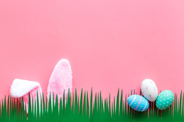 Easter concept. Eggs, Bunny's ears and grass on pink background top-down copy space