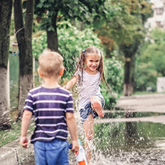 Fototapeta na wymiar Cute happy kids jumping in the puddles after warm summer rain, lifestyle outdoor, back view