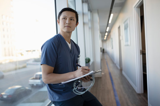 Thoughtful male nurse with clipboard in clinic corridor