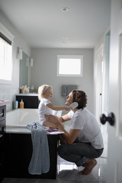 Cute toddler daughter brushing father s hair in bathroom
