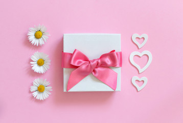 White gift box, daisies and hearts on a light pink background