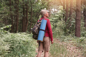 Traveler hiking through deep forest, stops near trees, looking up, sees strange bird, wearing