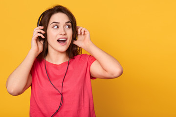 Close up portrait of beautiful young woman listening to music by headphones and singing, keeping...