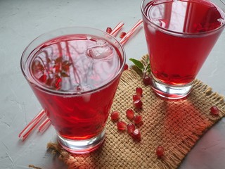 In a transparent glass, pomegranate juice with ice and mint. On a gray background are pomegranate seeds. Healthy eating