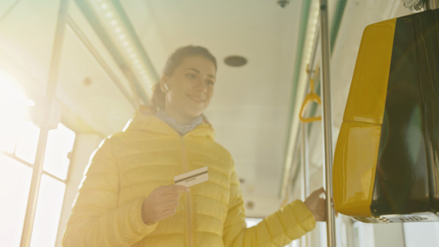 Young stylish woman using electronic ticket punching machine in public transport. Girl paying conctactless with bank card for the public transport in the tram