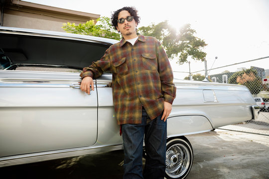 Portrait confident, cool Latinx man leaning on low rider in parking lot