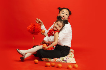 Hugging, smiling happy, holding lanterns. Happy Chinese New Year 2020. Asian mother and daughter portrait on red background in traditional clothing. Celebration, human emotions, holidays. Copyspace.