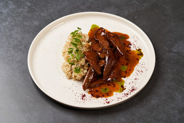 Baked lamb tongues with spicy bulgur porridge in a white plate
