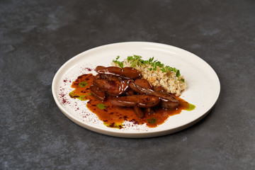 Baked lamb tongues with spicy bulgur porridge in a white plate
