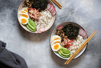 Poke bowl or sushi bowl with crab, rice, avocado, wakame seaweed, egg, radish and sesame seeds. Healthy clean eating. Traditional Hawaiian cuisine. Top view, flat lay, gray background