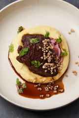 Stewed veal cheeks with mashed potatoes on a white plate, close-up.