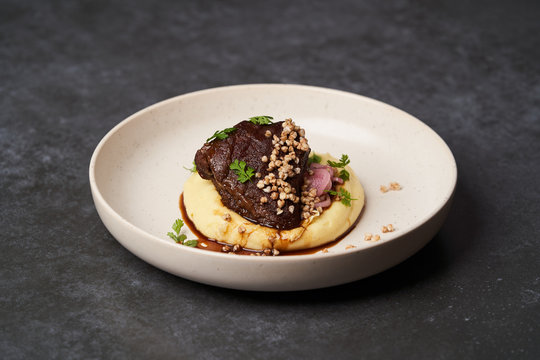 Stewed veal cheeks with mashed potatoes on a white plate, close-up.