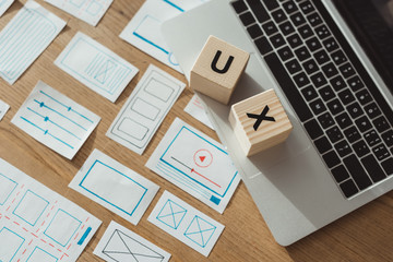High angle view of cubes with ux letters on laptop with website wireframe sketches on wooden table