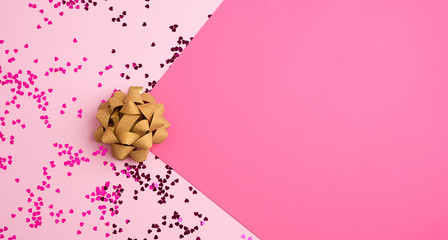 golden bow and shiny multi-colored round confetti scattered on a pink background