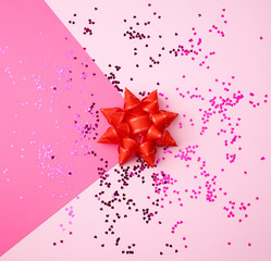 red bow and shiny multi-colored round confetti scattered on a pink background