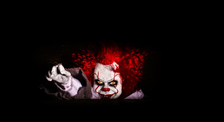 the evil clown killer peeps out of cover. horror. halloween concept. evil look.