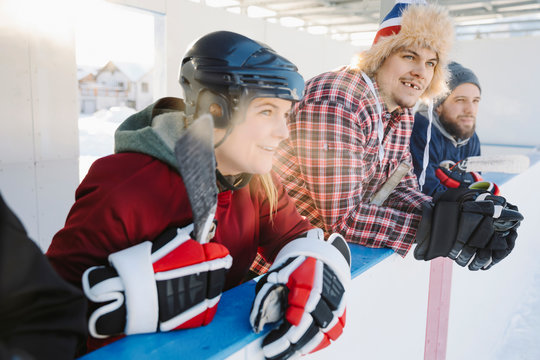 Friends watching outdoor ice hockey match from sideline bench