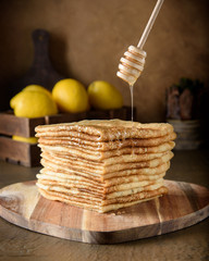 Honey from a spoon flows down on a stack of folded russian pancakes blini on a wooden board on a...