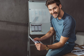 Designer smiling at camera while holding mobile website template in designer studio