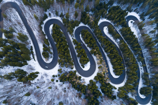Drone overhead shot of curved road in winter mountain landscape. Aerial view of forest and trees with a winding street surrounded by snow