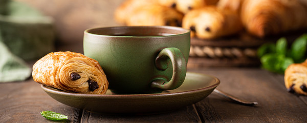 Green cup of tea with mini chocolate bun, puff pastry on old wooden table. Tasty tea break concept,...