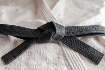 Fotobehang Black judo, aikido, or karate belt, tied in a knot,  laying on martial art uniform © marritch