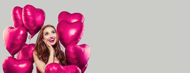 Young model woman having fun and holding pink heart balloons on gray background