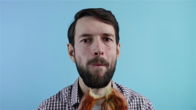 bearded man biting and eating pretzel on blue background portrait shot